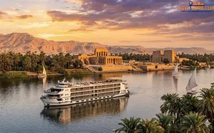 Beit Khufu – Aswan Luxor Cruise A Nile cruise ship sailing past temples and palm trees at sunset