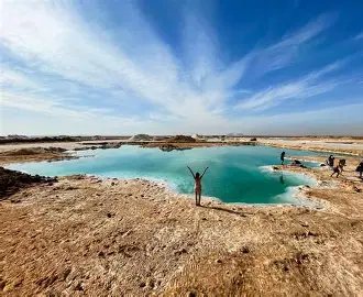 Beit Khufu – Siwa A visitor standing by a turquoise salt lake in Siwa Oasis